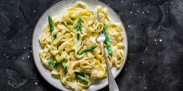 su sfondo nero un piatto bianco con pasta con asparagi croccanti e cremosi
