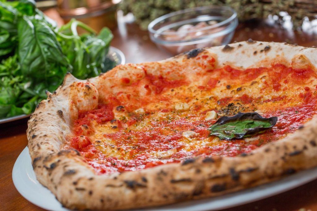 La pizza marinara: la ricetta perfetta per chi è a dieta 4 Su tavolo di legno primo piano di piatto con la pizza marinara e origano