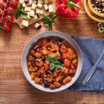 Caponata siciliana: la ricetta tradizionale fatta in casa 1 Caponata siciliana in ciotola con melanzane, peperoni, sedano, olive e basilico su tavolo in legno.