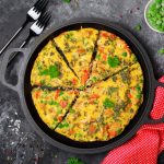 su base scura, una teglia tonda con manici e dentro una frittata a spicchi, accanto, due forchette