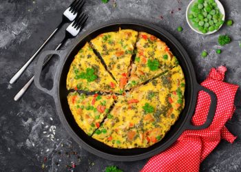 su base scura, una teglia tonda con manici e dentro una frittata a spicchi, accanto, due forchette