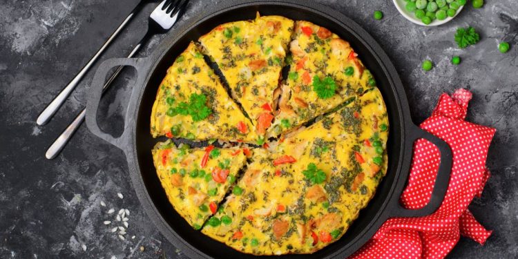 su base scura, una teglia tonda con manici e dentro una frittata a spicchi, accanto, due forchette