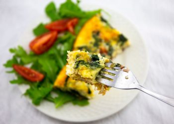 ricette con frittata: su base chiara un piatto tondo con una fetta di frittata, foglie di insalata e spicchi di pomodoro