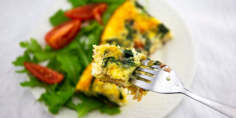 ricette con frittata: su base chiara un piatto tondo con una fetta di frittata, foglie di insalata e spicchi di pomodoro