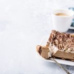 Semifreddo al caffè: la ricetta facile senza uova e panna 1 Fetta di semifreddo al caffè a strati con base scura, ciuffi di crema, cacao e granella, servita accanto a una tazza di caffè.