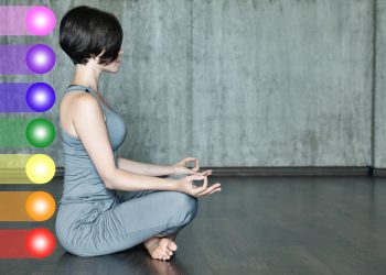 Donna seduta in posizione semplice con i colori dei 7 chakra dietro di lei