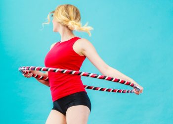 Donna su sfondo blu con shorts e maglia rossa con un hula hoop che fa girare attorno alla vita