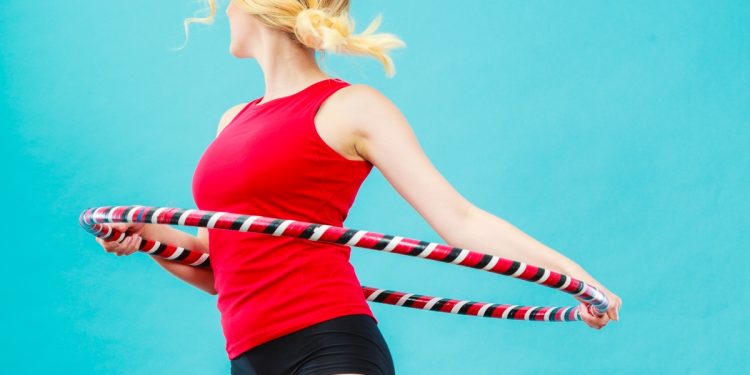 Donna su sfondo blu con shorts e maglia rossa con un hula hoop che fa girare attorno alla vita