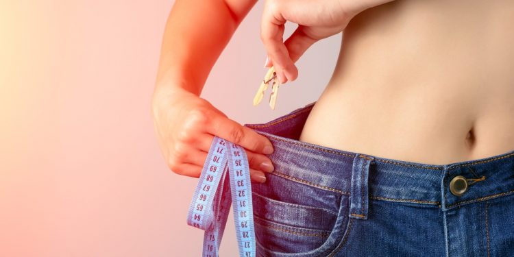 Donna con jeans che prende una molletta per stringere il jeans perché è dimagrita e ha raggiunto il peso ideale