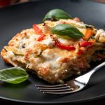 primo piano di un piatto nero con una porzione di lasagne con zucchine