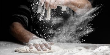 in primo piano delle mani che impastano e usano la farina di frumento