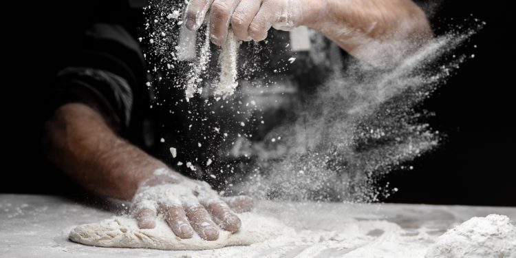 in primo piano delle mani che impastano e usano la farina di frumento