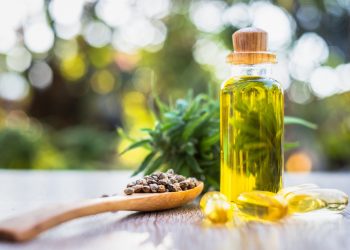 una boccetta in vetro contenente olio di canapa e un cucchiaio di legno che contiene semi di olio di canapa