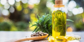 una boccetta in vetro contenente olio di canapa e un cucchiaio di legno che contiene semi di olio di canapa