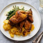 Pollo al forno con patate: ricetta facile e saporita 1 su tavolo, in cucina un piatto bianco visto dall'alto con pollo al forno con patate e fagiolini. Accanto bicchiere con vino bianco 1 forchetta e un coltello.