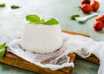 latticini, una ricotta su un tagliere con una foglia id basilico