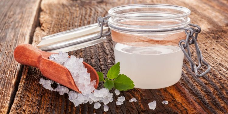 su tavolo di legno, contenitore di vetro ermetico con kefir d'acqua e accanto granuli per fare la ricetta in casa