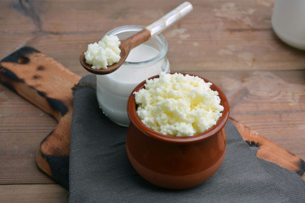 su tavolo da cucina tagliere di legno con un contenitore di kefir di latte e un barattolo con latte e un cucchiaino di legno