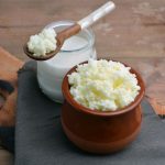 su tavolo da cucina tagliere di legno con un contenitore di kefir di latte e un barattolo con latte e un cucchiaino di legno