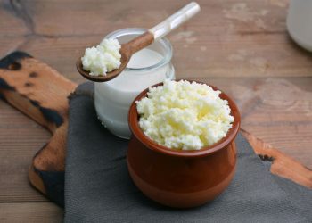 su tavolo da cucina tagliere di legno con un contenitore di kefir di latte e un barattolo con latte e un cucchiaino di legno