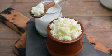su tavolo da cucina tagliere di legno con un contenitore di kefir di latte e un barattolo con latte e un cucchiaino di legno