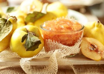 mela cotogna: su piano di legno varie mele cotogne intere e a spicchi e una ciotola di vetro con le mele cotte