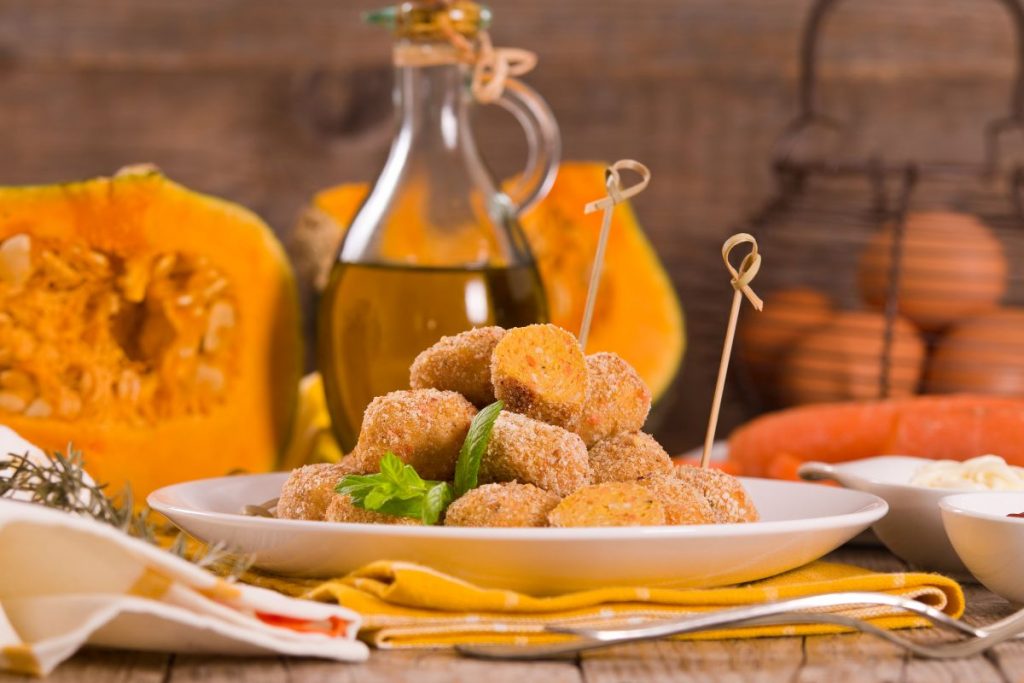 Polpette di zucca, il secondo vegetariano completo e goloso 3 piatto bianco con polpette di zucca e spiedini, zucca aperta e flacone di olio sullo sfondo