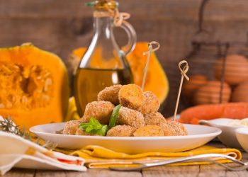 piatto bianco con polpette di zucca e spiedini, zucca aperta e flacone di olio sullo sfondo