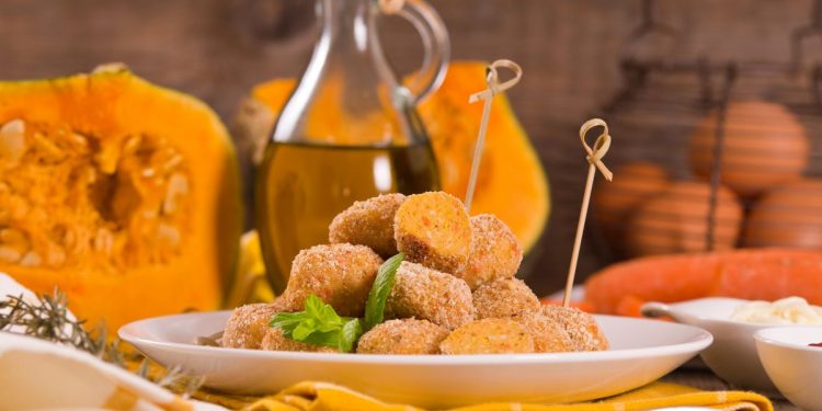 piatto bianco con polpette di zucca e spiedini, zucca aperta e flacone di olio sullo sfondo