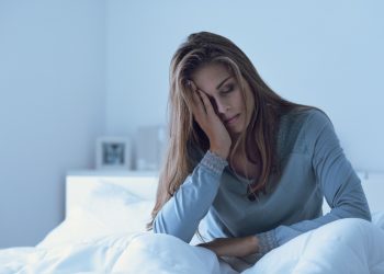 una donna dall'aspetto affaticato seduta su un letto per rappresentare la stanchezza cronica