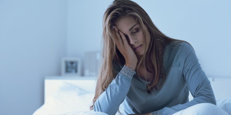 una donna dall'aspetto affaticato seduta su un letto per rappresentare la stanchezza cronica
