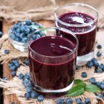 su tavolo di legno 2 bicchieri con succo di mirtillo e attorno mirtilli freschi