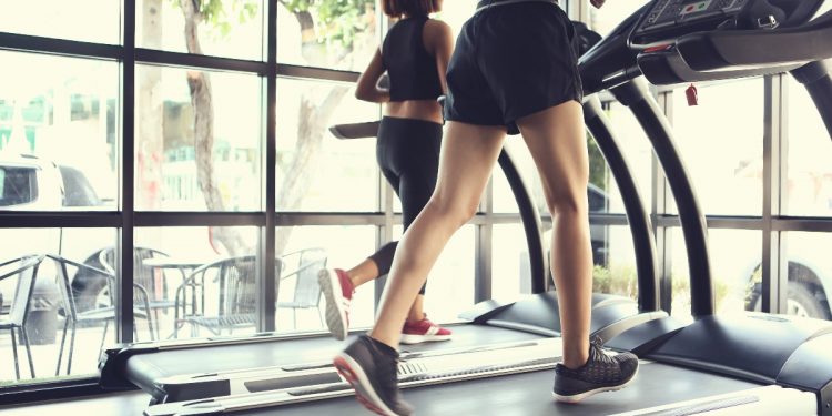 Gambe di una donna con gli shorts che si allena in palestra su un tapis roulant elettrico