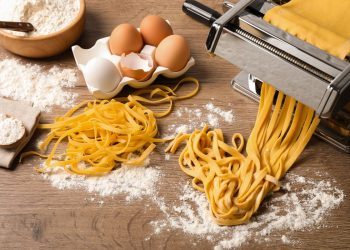 su un tavolo, una macchinetta per tirare la sfoglia della pasta fatta in casa, uova e farina
