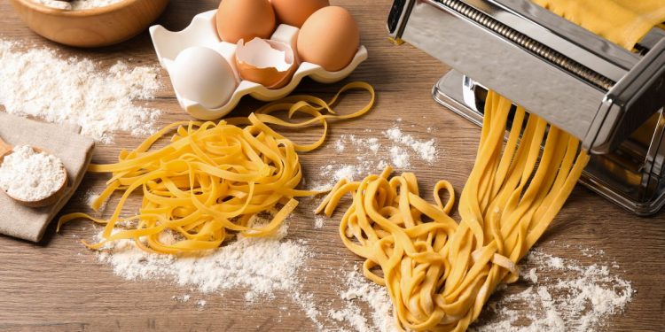 su un tavolo, una macchinetta per tirare la sfoglia della pasta fatta in casa, uova e farina