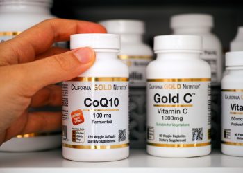 coenzima Q10, una mano che prende un flacone di integratore a base di Q10