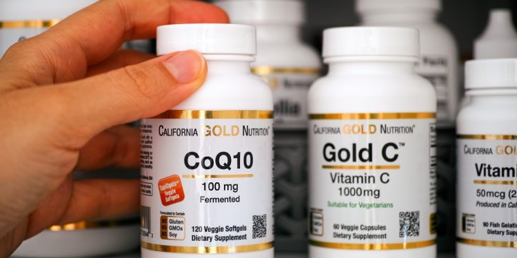coenzima Q10, una mano che prende un flacone di integratore a base di Q10