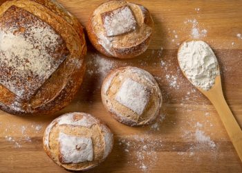 una pagnotta e tre pagnottine accanto a un mestolo di farina