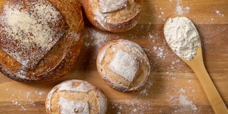 una pagnotta e tre pagnottine accanto a un mestolo di farina