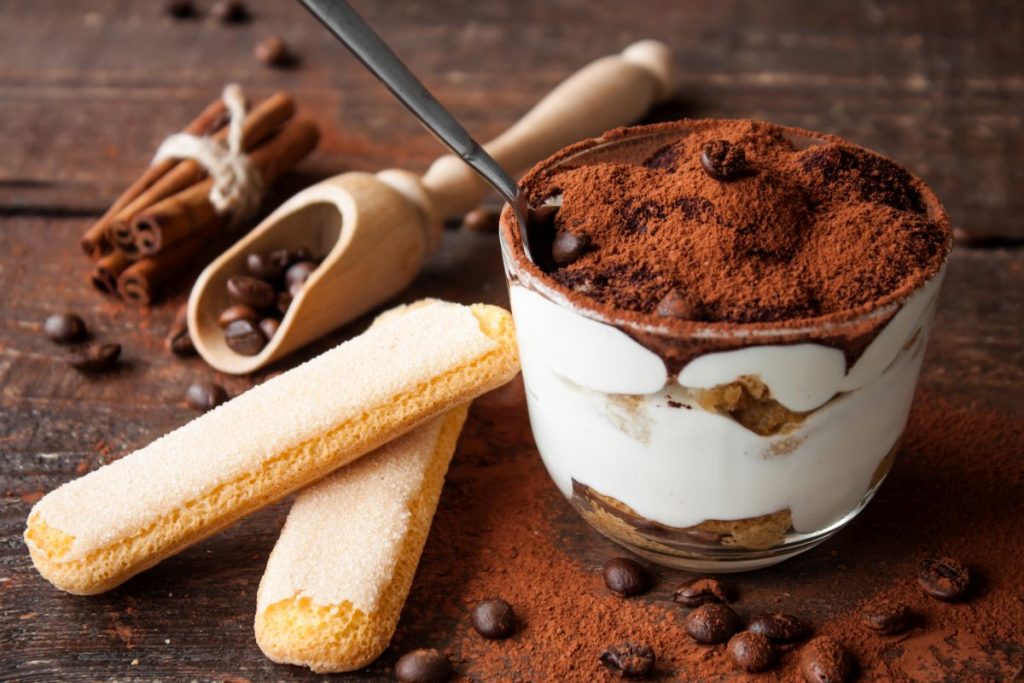 Dolci al cucchiaio: 41 ricette leggere e golose 1 su bas edi legno un bicchierino di tiramisù e dei savoiardi, chicchi di caffè sparsi