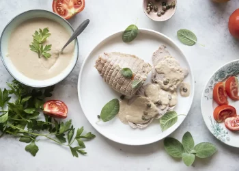 piatto tondo con vitello tonnato, scodella con salsa e pomodori sparsi intorno
