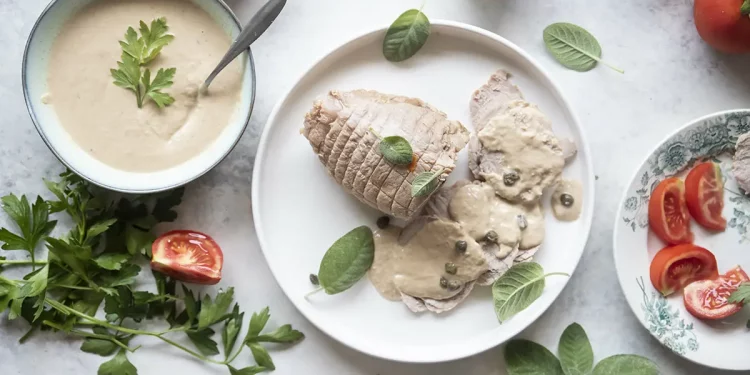 piatto tondo con vitello tonnato, scodella con salsa e pomodori sparsi intorno