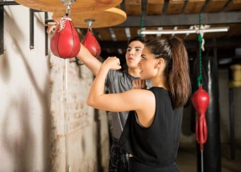 donna in palestra si allena con il pungiball o punching ball con il suo coach che gli spiega come fare