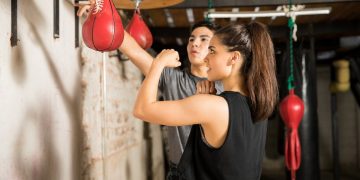 donna in palestra si allena con il pungiball o punching ball con il suo coach che gli spiega come fare