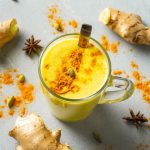 su tavolo di marmo, tazza trasparente con latte d'oro e attorno polvere di curcuma e zenzero e anice stellato