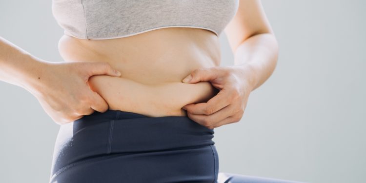 Donna in sovrappeso seduta che si tiene in mano il grasso addominale