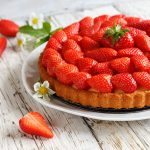 Crostata di fragole: 1 In primo piano su uno sfondo di legno chiaro c'è un piatto con la crostata di fragole e qualche fragola fresca intorno.