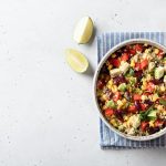 Quinoa con verdure: ricetta leggera e senza glutine 1 Im primo piano su un tavolo di marmo bianco in un piatto fondo c'รจ della quinoa con verdure. Sulla destra una forchetta e in alto a sinistra due spicchi di lime.