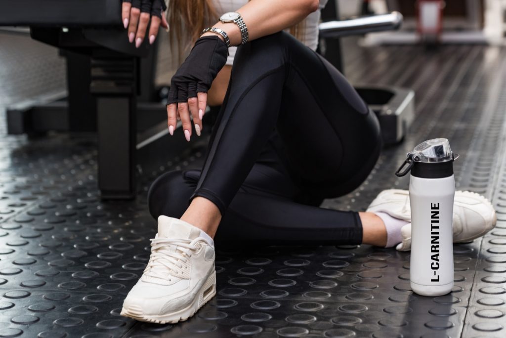 una giovane donna in palestra che tiene in mano una borraccia con la scritta L-carnitina