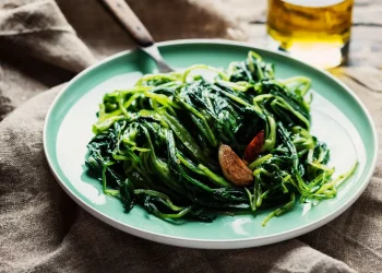 su un tavolo di legno piatto blu con la cicoria ripassata e accanto una bottiglia di olio d'oliva
